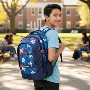 Young man with a blue floral-patterned backpack standing outdoors on a college campus.